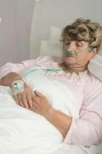 A patient lays in a hospital bed. A nasal cannula helps her receive oxygen from a machine