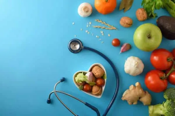 A stethoscope surrounded by health foods such as fruits, nuts, and vegetables.